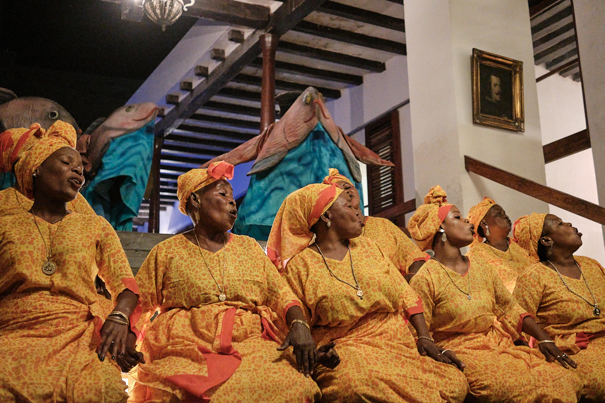 <# Local women sing, with Rare’s fish mascot dancing in the background #>